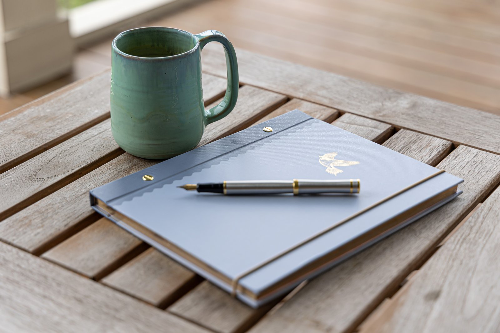 A green ceramic cup, journal, and pen in the morning light